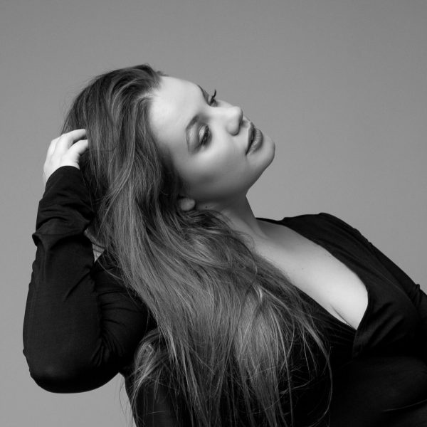 modelka siedząca na fotelu trzymająca się za włosy patrząca w bok na czarno białej fotografii