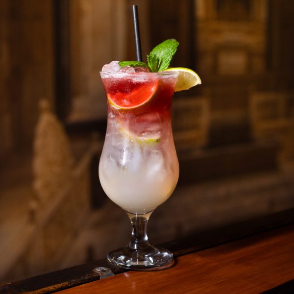 drink w wysokiej szklance w kolorze czerwono białej z limonką, mięta na drewnianym blacie